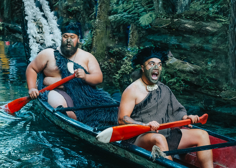 Two Maori warriors chanting from a wooden canoe in a stream at Mitai Maori Village one of the best experiences in New Zealand