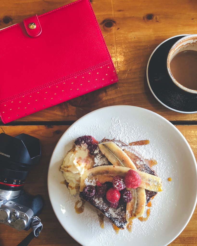 A plate of french toast, fuji camera, notebook and coffee on a cafe table